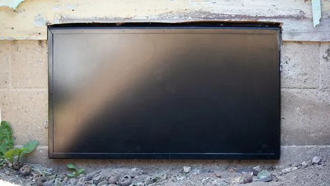 Black metal access door installed on a block foundation