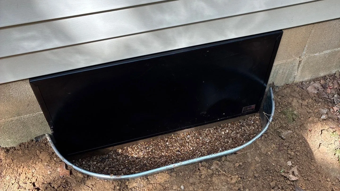 Black crawlspace access door installed in a foundation below vinyl siding