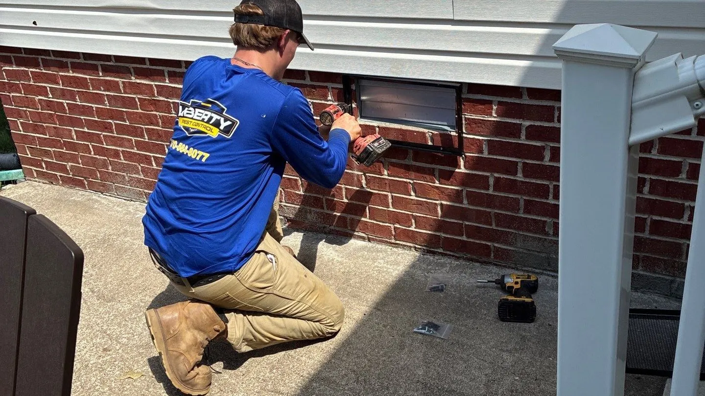 Service Specialist installing a vent guard over a foundation vent in a brick wall
