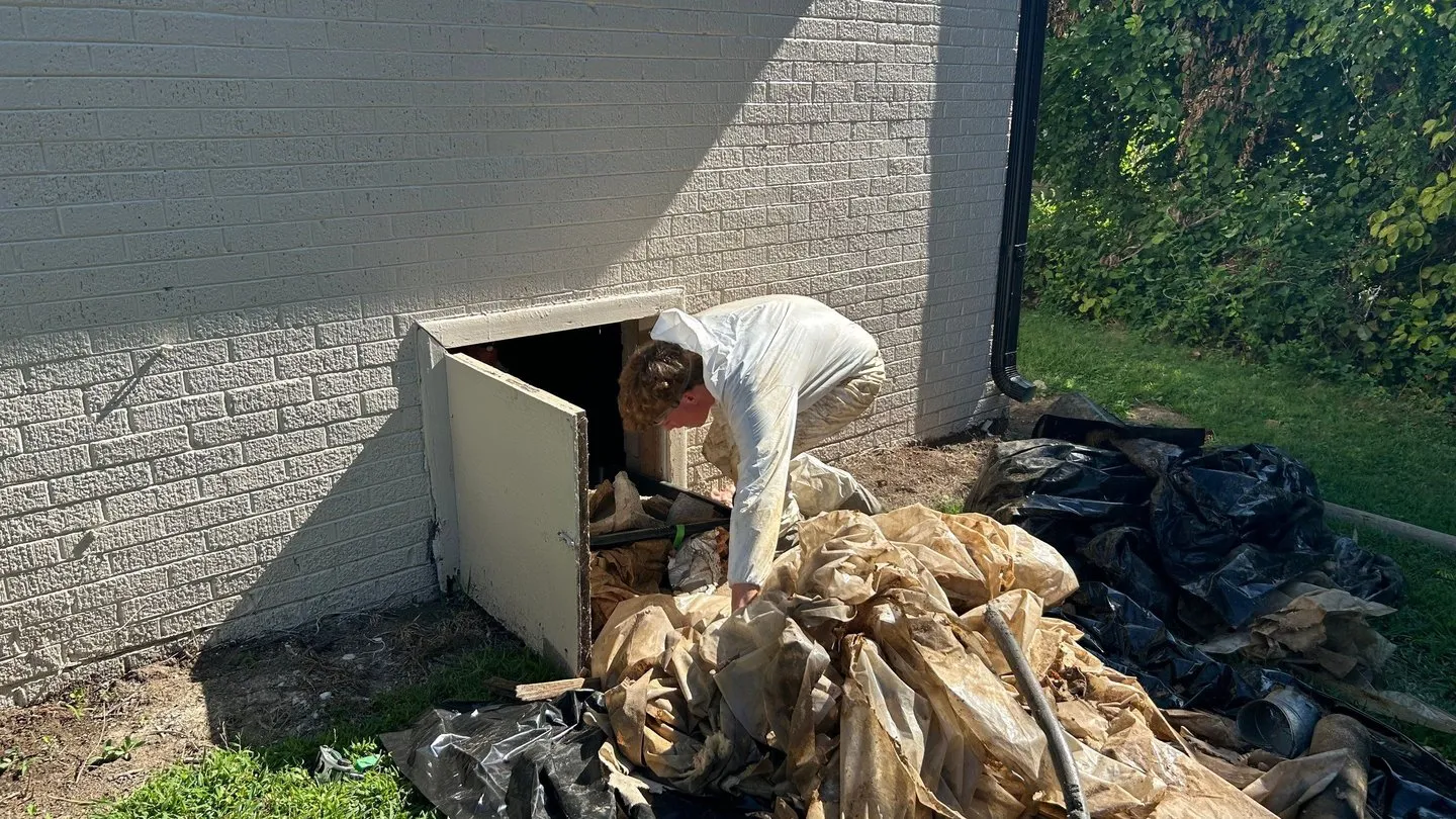 Worker pulling old plastic and debris out of a crawlspace door onto the lawn