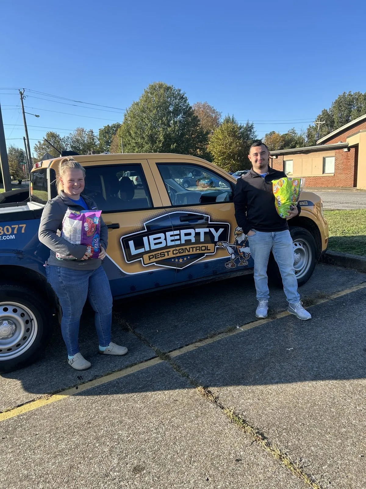 John Stopka and a helper holding bags of Halloween candy beside a Liberty Pest Control truck