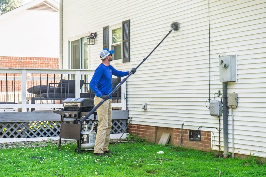 Liberty Service Specialist using a long pole brush to remove spider webs from a home's eaves