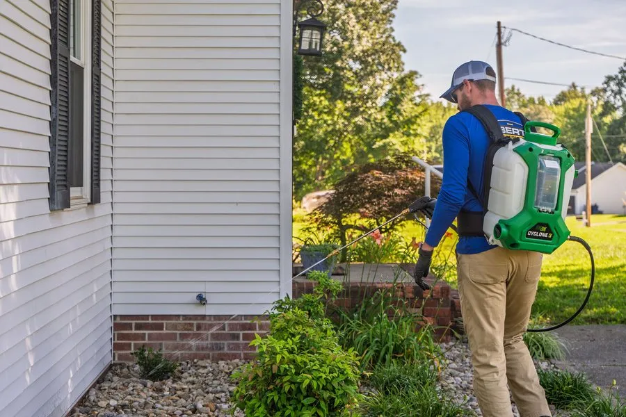 Liberty Service Specialist treating the foundation beds around a home with a backpack sprayer