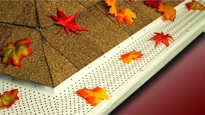 Perforated gutter guard installed along a roof edge, with leaves resting on top