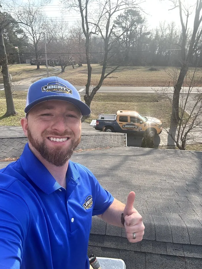 Liberty Pest Control Service Specialist giving a thumbs up from a rooftop, with a Liberty truck parked below